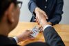 Businesspeople shaking hands to receive banknote money and terms Businesspeople shaking hands to receive banknote money and terms of contract from bribe employer in signing contract while making corruption